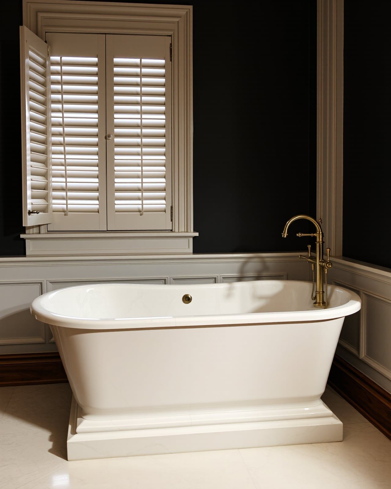 A freestanding cream-marble soaker tub on a book-matched marble plinth in a restored Brooklyn Heights brownstone bathing suite, a polished brass floor filler and walnut millwork warm in candlelight